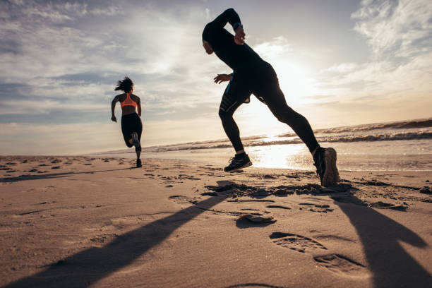 Rear view of two people sprinting on the beach. Man and woman doing running training on the shore in morning.